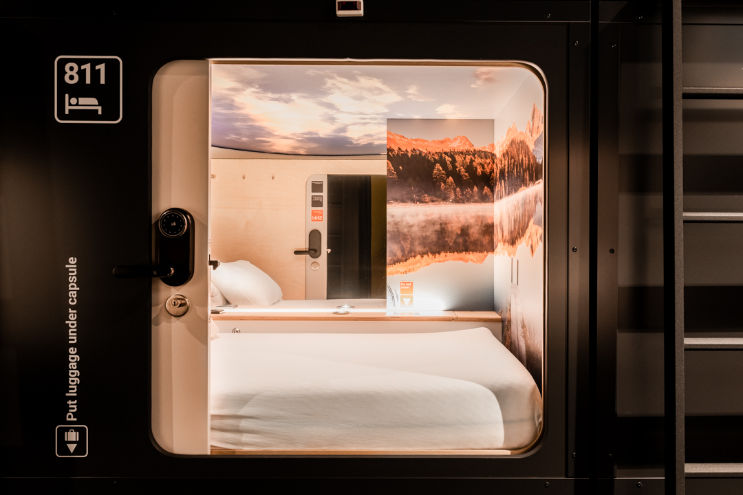 Rows of sleeping capsules along a lit corridor, the shared form behind the capsule hotels group
